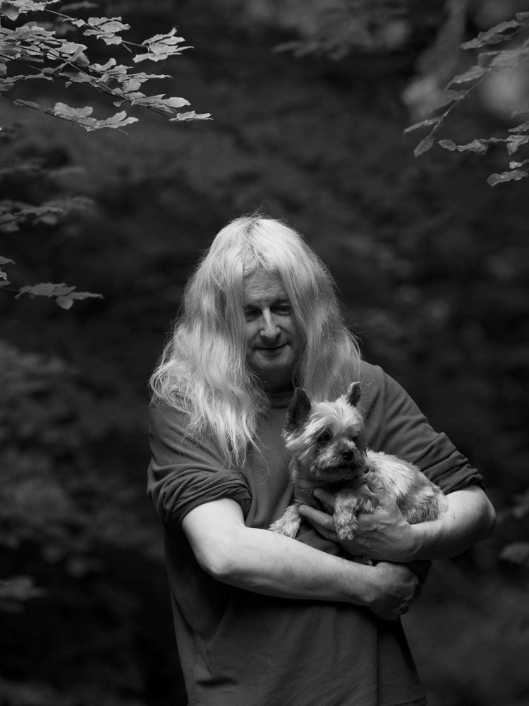 Photography by Mario Popham, for wigan arts festival, photographing nature during lockdown. A black and white photograph of a person in nature, holding a dog.